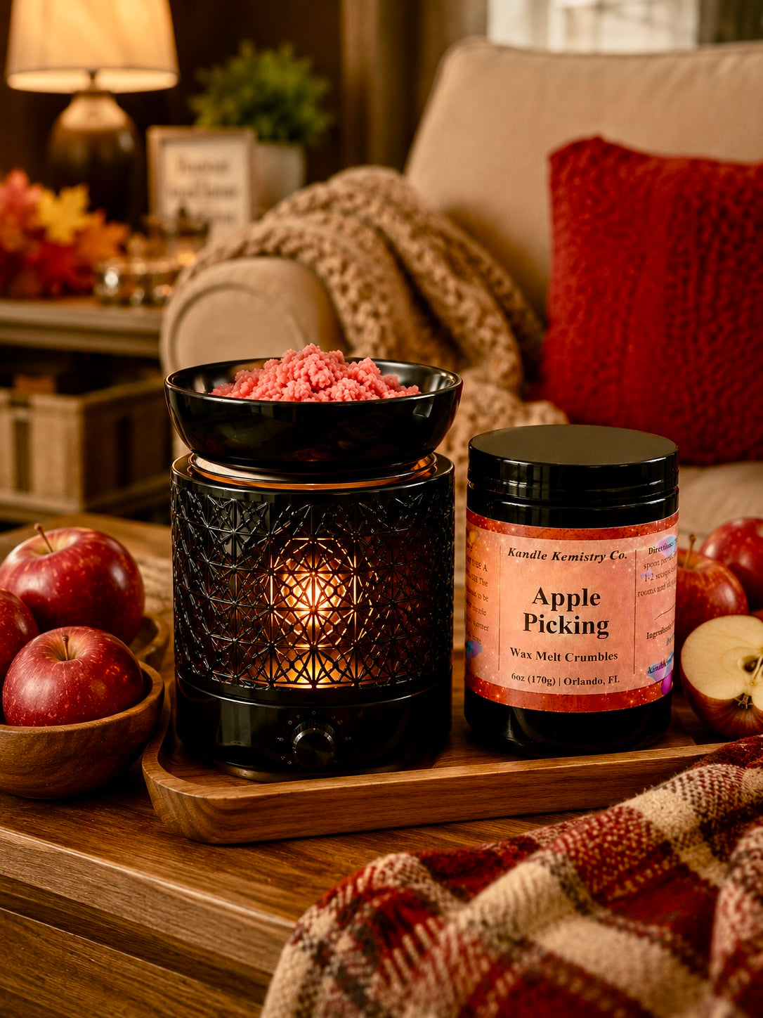 A cozy home setting featuring a black wax melt warmer with a glowing candle inside, next to a jar of Kandle Kemistry Co. Apple Picking wax melts.