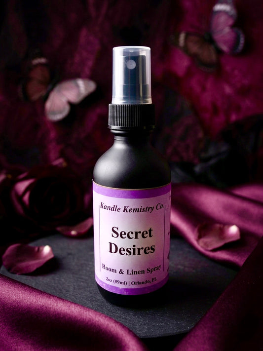 Bottle of 'Secret Desires' room & linen spray with a purple label on a dark surface.