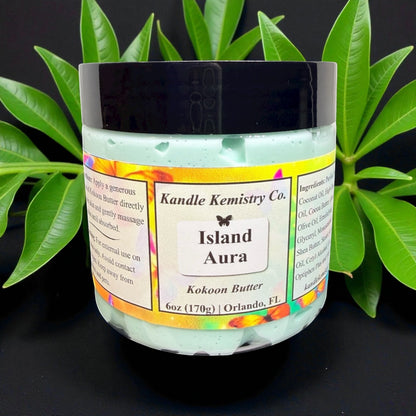Jar of body Butter with 'Island Aura' label on a dark background with green leaves.