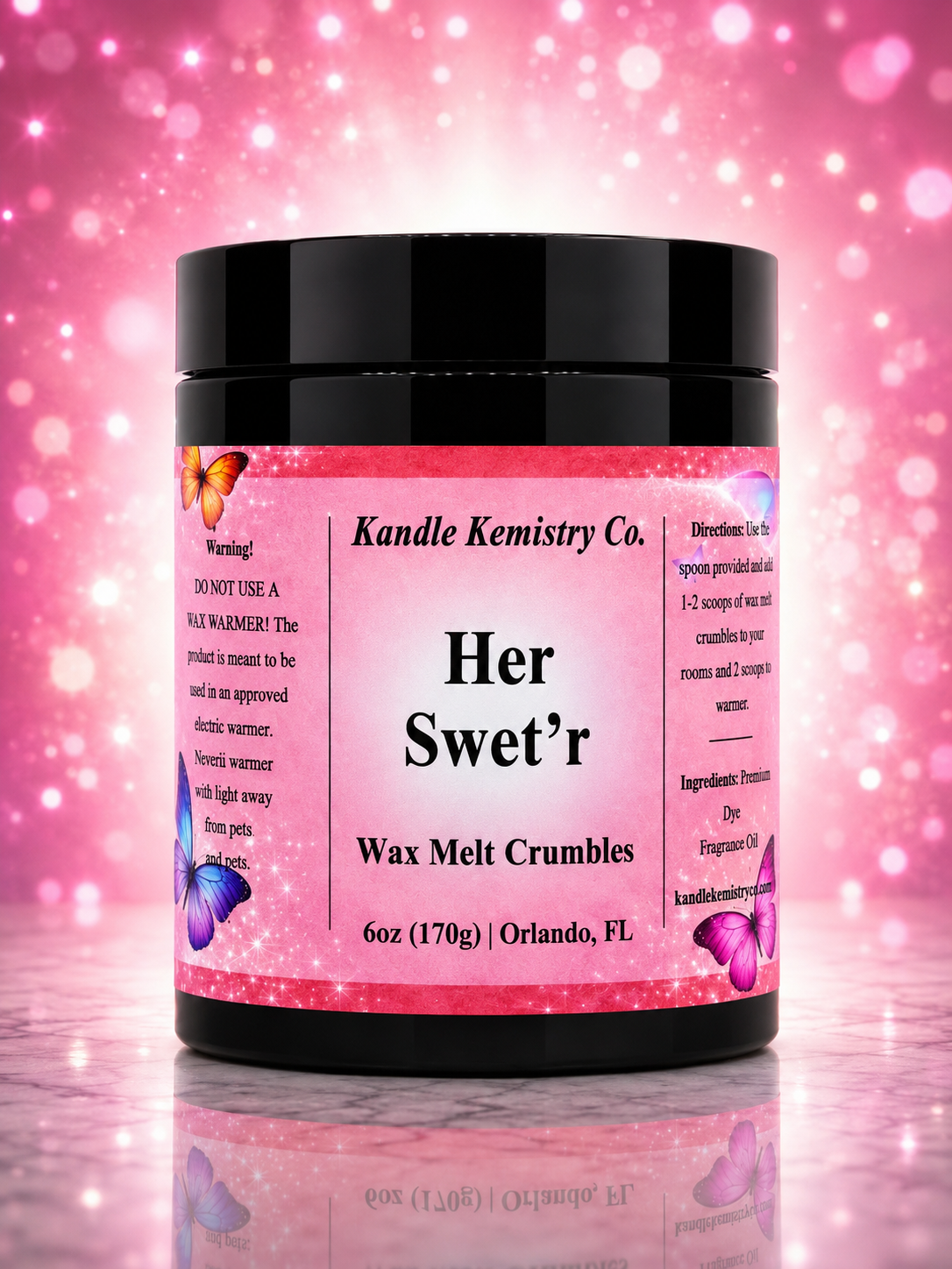 A black plastic jar of Kandle Kemistry Co. 'Her Swet'r' Wax Melt Crumbles, featuring a pink glittery label with purple butterflies, set against a pink bokeh background.