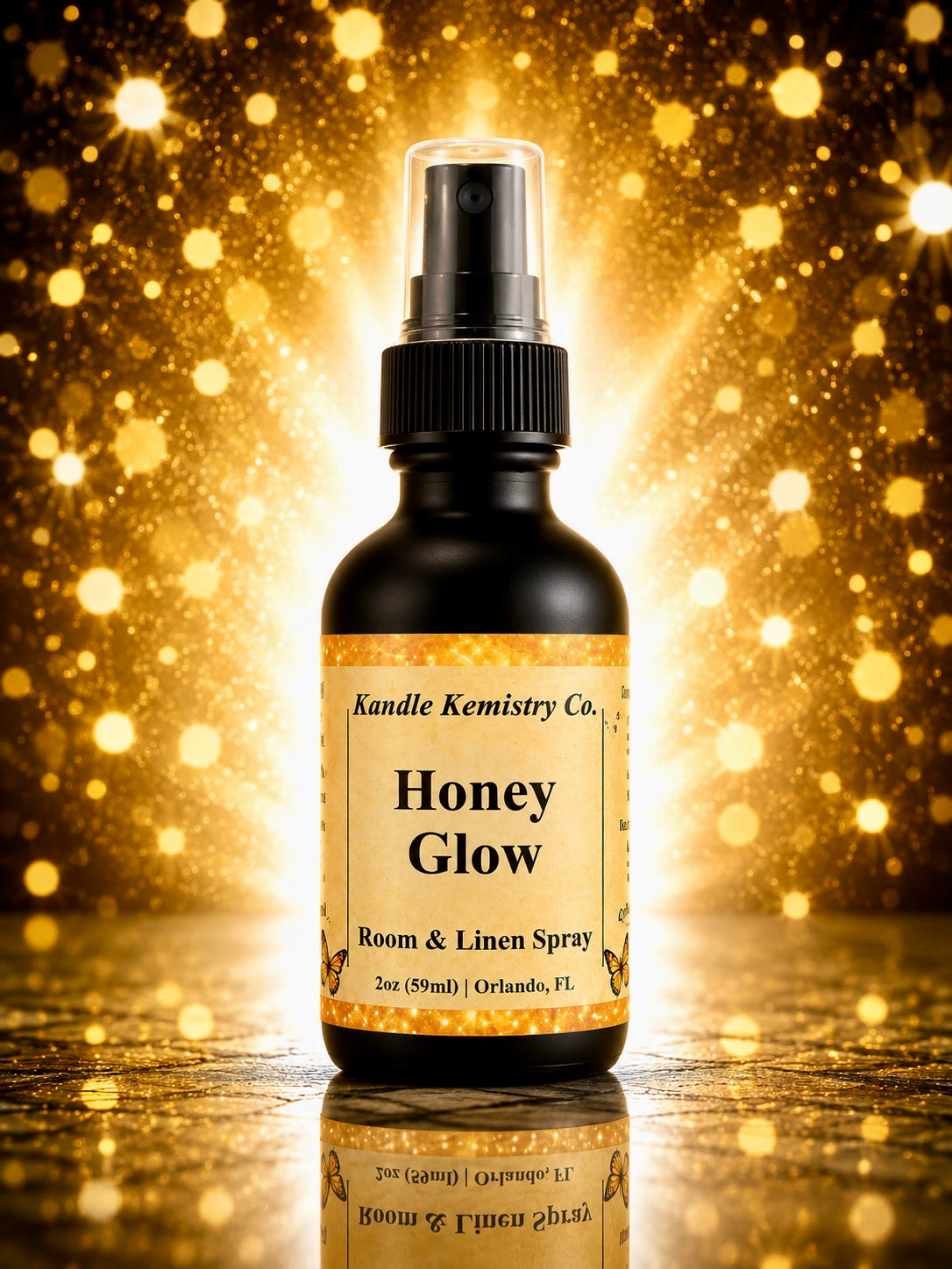 A bottle of Honey Glow Room & Linen Spray by Kandle Kemistry Co. The product is in a black glass bottle with a black spray pump and a beige label, set against a sparkling golden bokeh background with a reflective surface below.