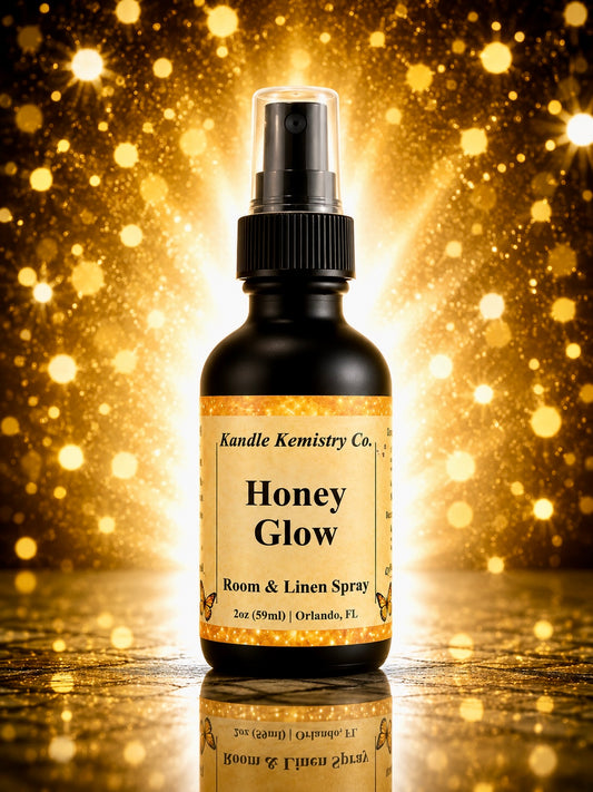A bottle of Honey Glow Room & Linen Spray by Kandle Kemistry Co. The product is in a black glass bottle with a black spray pump and a beige label, set against a sparkling golden bokeh background with a reflective surface below.