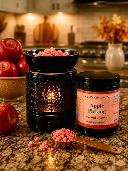 A jar of Kandle Kemistry Co. Apple Picking wax melt crumbles and a black electric wax warmer, styled on a kitchen countertop with red apples and warm background lighting.