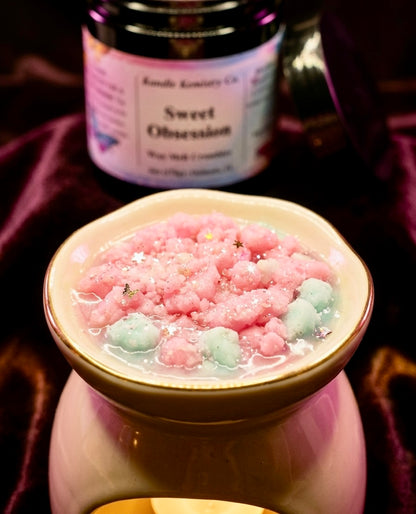 Pink and teal wax melt crumbles melted in a pink wax melt warmer with a jar labeled 'Sweet Obsession' in the background.