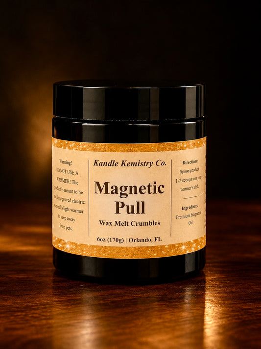 A black jar of Kandle Kemistry Co. Magnetic Pull Wax Melt Crumbles, set on a dark wooden surface with a warm, atmospheric background.