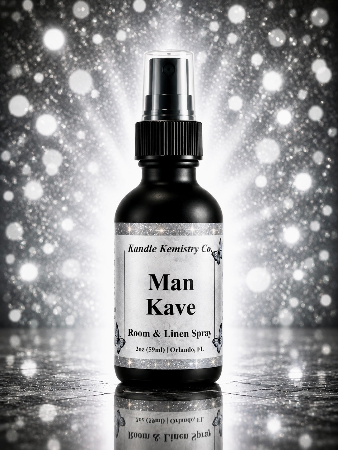 A 2 oz room and linen spray bottle from Kandle Kemistry Co. labeled 'Man Kave', shown against a sparkling silver and black bokeh background with a reflective surface below.