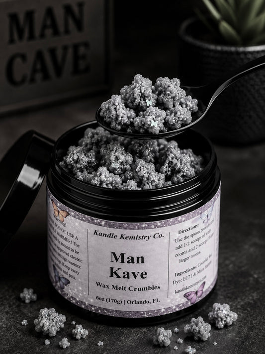 An open black jar of Man Kave Wax Melt Crumbles by Kandle Kemistry Co. sits on a dark surface with a spoon holding some of the crumbly product above the jar.