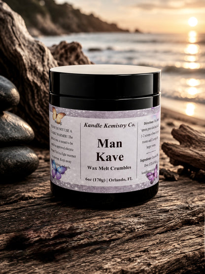 A jar of Kandle Kemistry Co. 'Man Kave' Wax Melt Crumbles sits on a weathered log by the ocean at sunset.