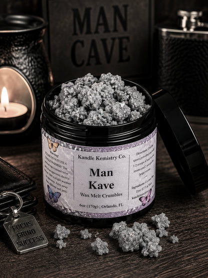 An open black jar of Man Kave Wax Melt Crumbles by Kandle Kemistry Co. sits on a dark wooden surface with a few crumbles spilled in front.