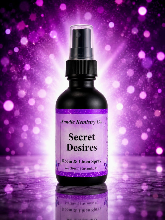 A black spray bottle labeled 'Secret Desires' by Kandle Kemistry Co., shown against a purple glittery bokeh background with a reflective surface below.