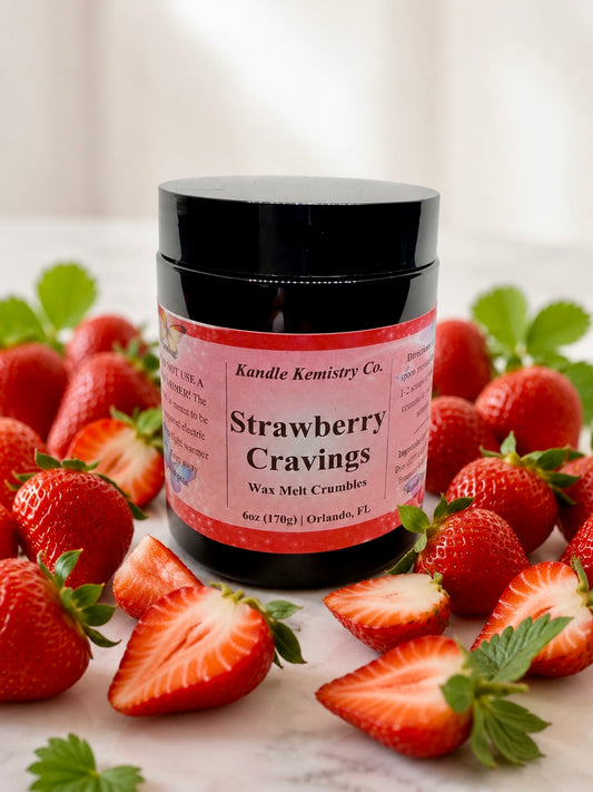 A jar of Kandle Kemistry Co. Strawberry Cravings Wax Melt Crumbles, surrounded by fresh whole and sliced strawberries on a light marble surface with a soft, bright background.