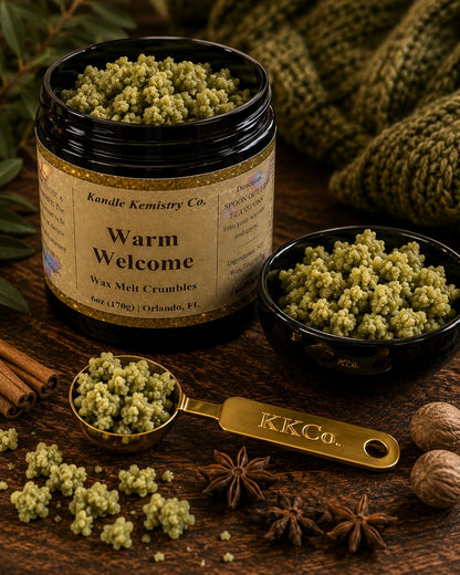 A jar of Kandle Kemistry Co. 'Warm Welcome' wax melt crumbles alongside a small bowl, a measuring scoop, and scattered crumbs on a rustic wooden surface with cinnamon sticks, star anise, walnuts, and a knitted green textile in the background.